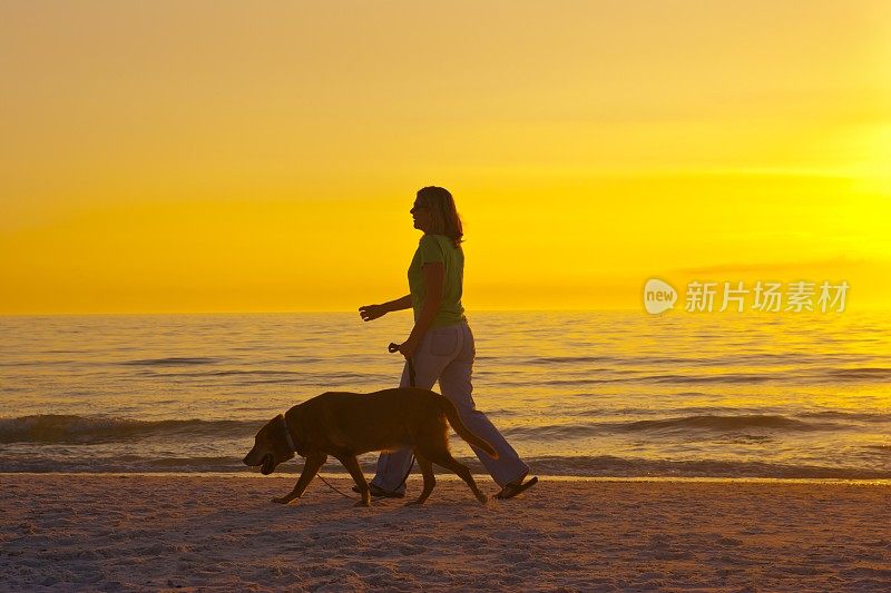 一个女人在日落时分的海滩上遛狗