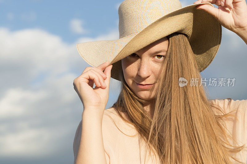 美丽的年轻女子与草帽肖像在牧场