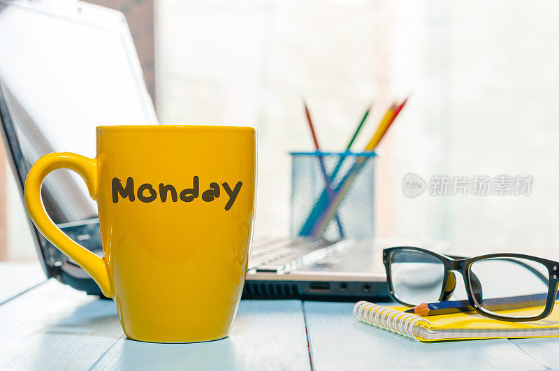 星期一写在黄色咖啡杯或茶杯上的木板桌子上，工作场所，办公室阳光早晨的背景