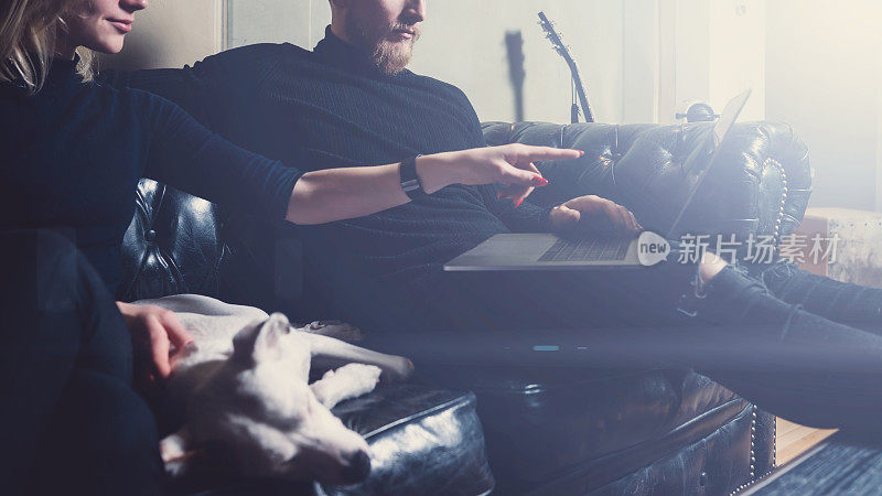 留胡子在家工作的同事。男人坐在复古沙发上，用着现代笔记本。一个女人用手指着笔记本电脑的屏幕。水平,视觉效果。