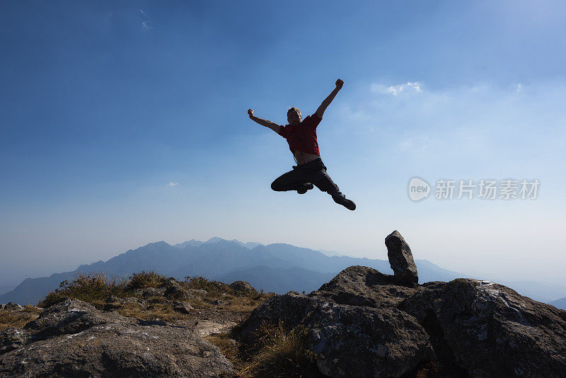 在山顶上举起手臂跳跃的男人