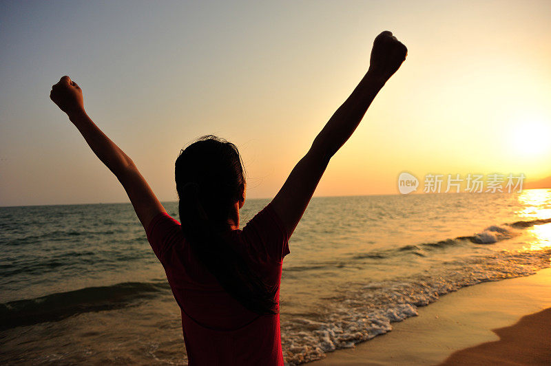 欢呼的女人在海边向夕阳张开双臂
