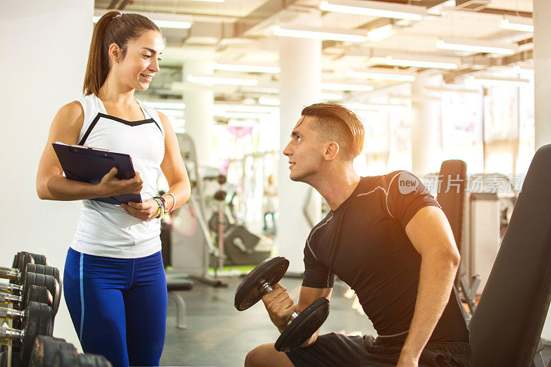 女性私人教练在健身房向她的男性客户展示锻炼报告。