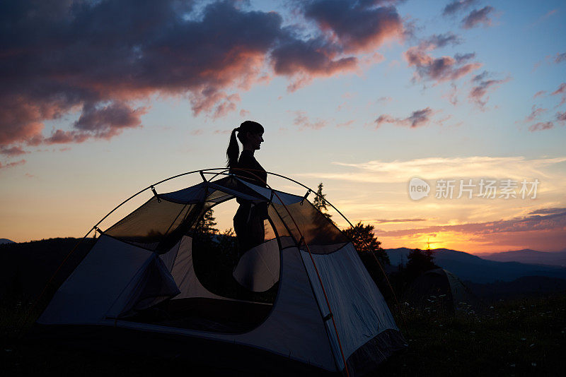 一个迷人的女孩的侧影站在帐篷附近，在傍晚的天空下黎明