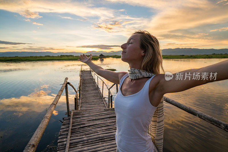 幸福的女人双臂伸展在湖桥日落，缅甸