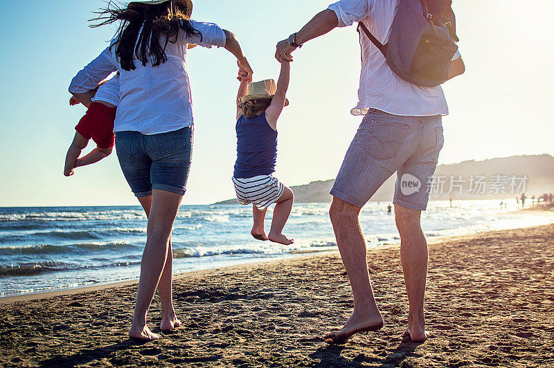 幸福的年轻的家庭在日落时在海滩上跑步