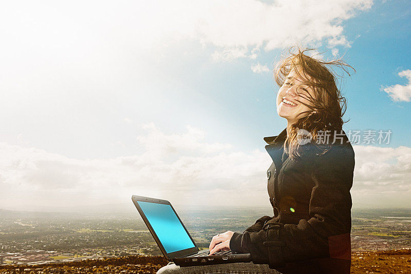 我可以在任何地方工作!带着笔记本电脑在山顶微笑的女孩