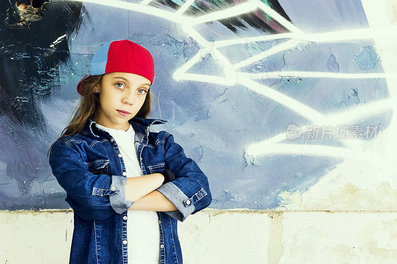 可爱的年轻金发少女在一个棒球帽和牛仔衬衫的石墙背景。