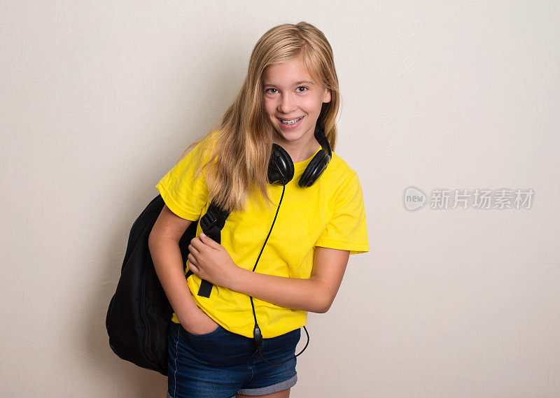 十几岁的女孩学生在黄色t恤与背包和耳机微笑。教育。