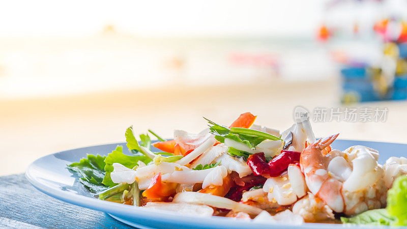 辛辣海鲜沙拉是一种泰式健康食物，它将粉丝、鱿鱼、虾、洋葱、辣椒和香草混合在泰国街头小吃的木桌上