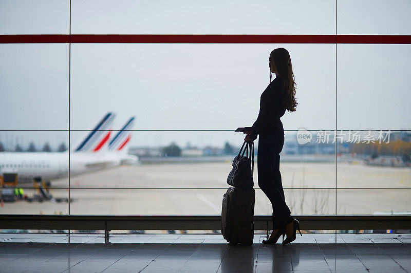 一个女人在机场，透过窗户看飞机