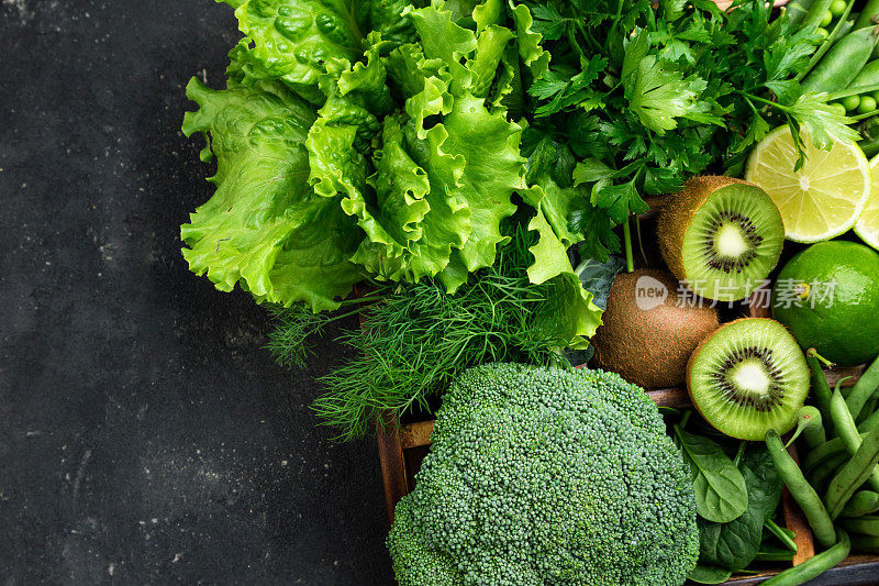 绿色蔬菜。椰菜，菠菜，猕猴桃，生菜，欧芹，莳萝，芦笋豆放在深色的混凝土桌上。素食