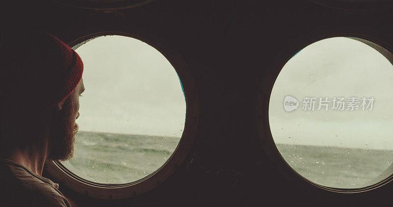 在波涛汹涌的海面上，一个人在一艘船的舷窗旁
