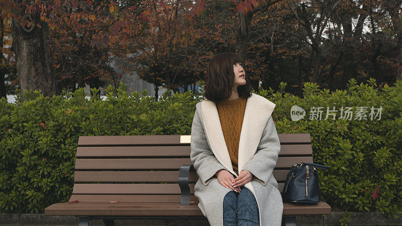 秋天里，一个年轻女子坐在公园的长椅上