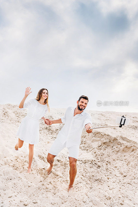 好玩的年轻夫妇用单脚架和智能手机在沙漠中自拍