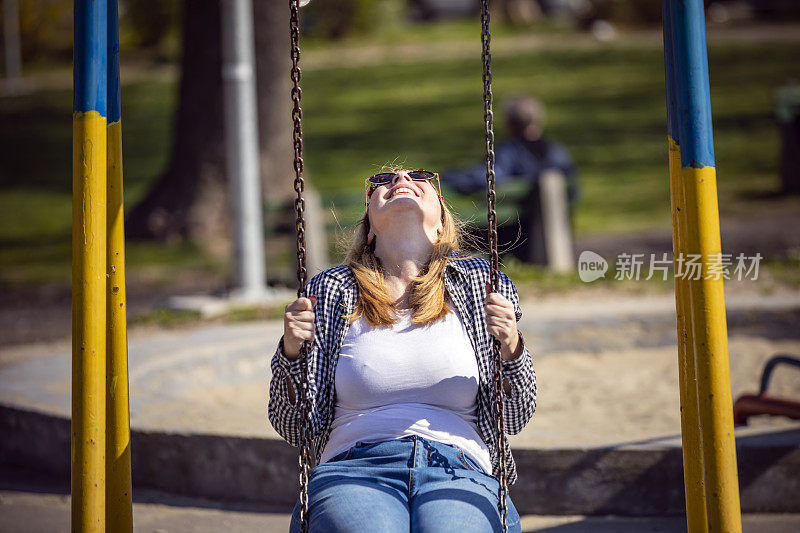 女嬉皮人在阳光明媚的日子里享受，在公共游乐场荡秋千