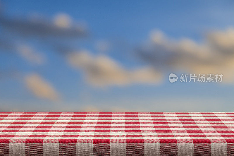 背景:红色和白色格子桌布与蓝天和云的背景