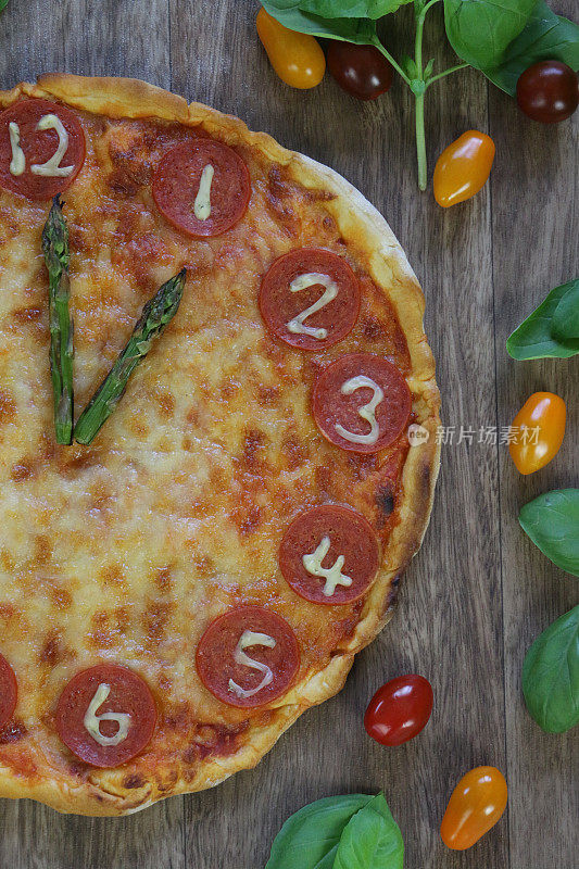 这是一个自制的披萨时钟，上面有意大利辣香肠片、马苏里拉奶酪和芦笋作为时钟指针，显示时间是13:00和1点，这是意大利披萨餐厅为孩子们的生日聚会食物而制作的儿童披萨时钟
