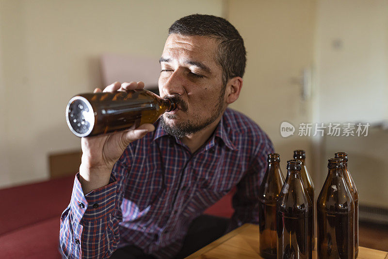 年轻悲伤的醉酒男子喝啤酒和酒精感到浪费，孤独和绝望的痛苦和情绪压力。人与酗酒、上瘾和男人抑郁的概念。