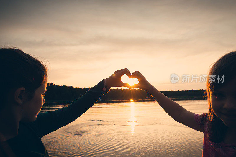 女孩的手在心的形状在夕阳湖上