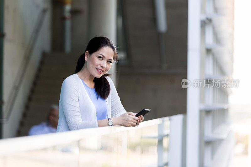 女人一边站在阳台上拿着手机一边看镜头