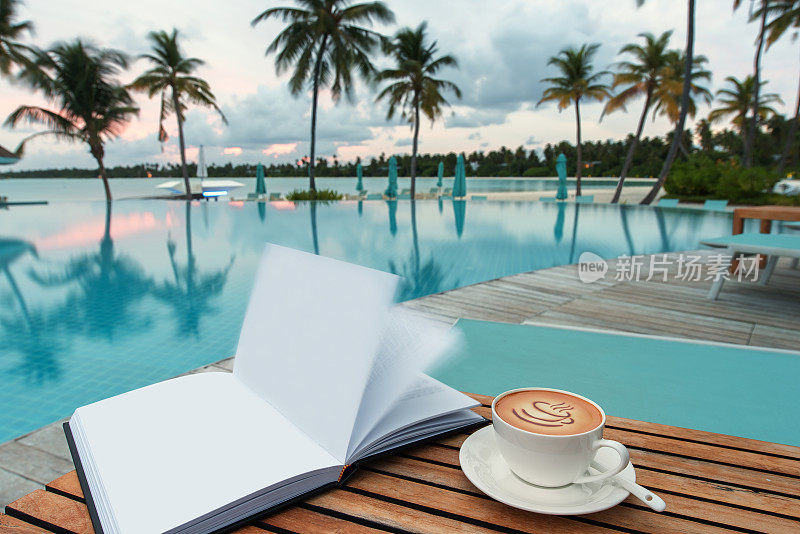 早上在游泳池旁边的木桌上放着一杯咖啡和一本书