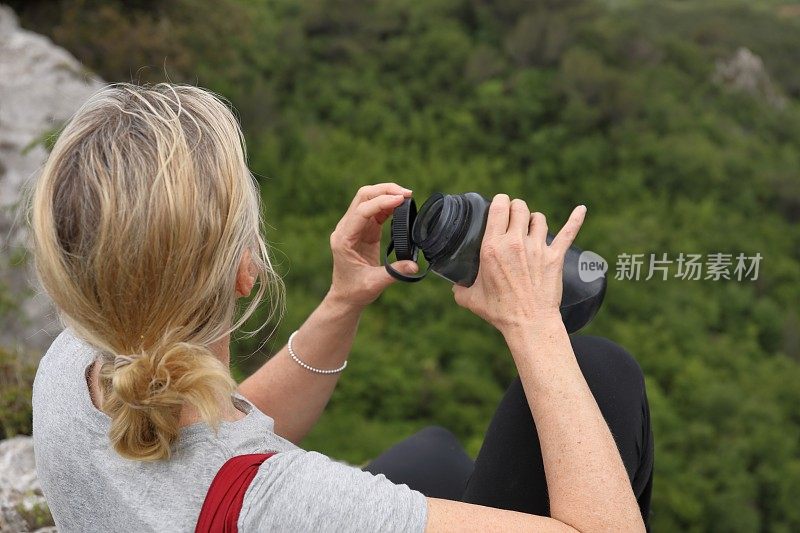 女性徒步旅行者在山谷上方放松，喝着水