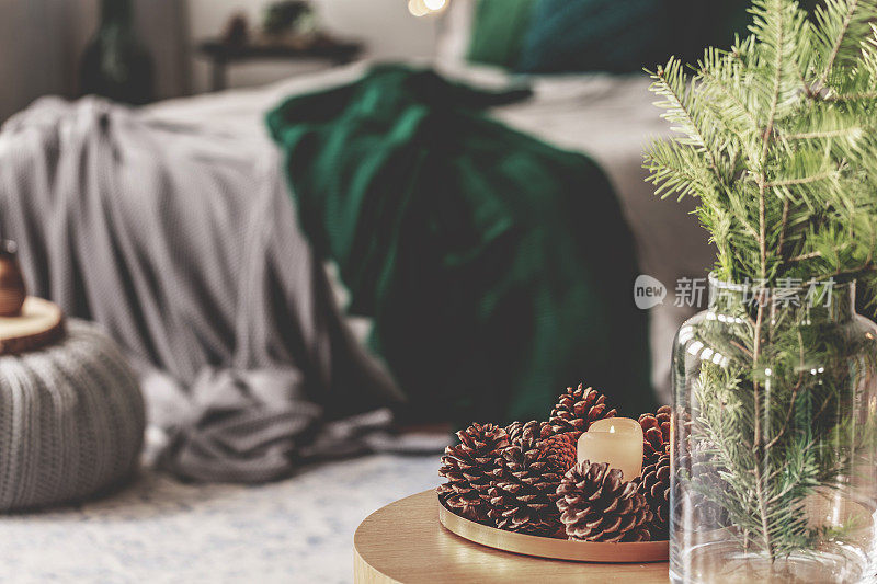 在优雅的卧室内部，咖啡桌上的玻璃花瓶和一盘球果和鲜花，灰色的床和翠绿色的床上用品