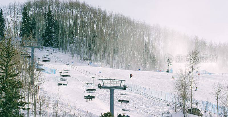 滑雪者和单板滑雪者乘坐滑雪缆车，人们在冬季科罗拉多山滑雪胜地的斜坡上滑雪(比弗溪)