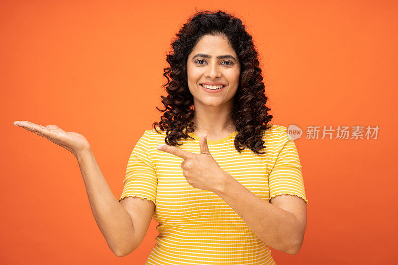 女孩漂亮的食指肖像，指示买家新产品在橙色背景的股票照片上张开的手