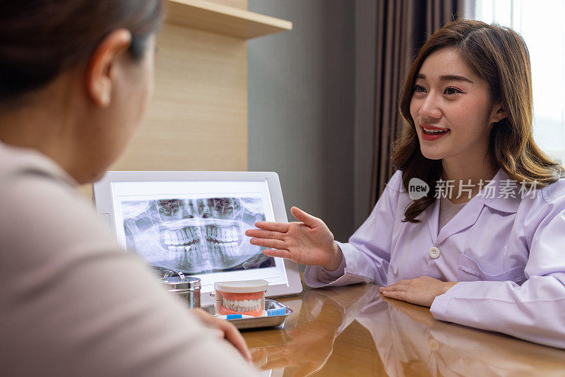 亚洲女牙医在办公桌前拿着牙齿x光片与病人交谈