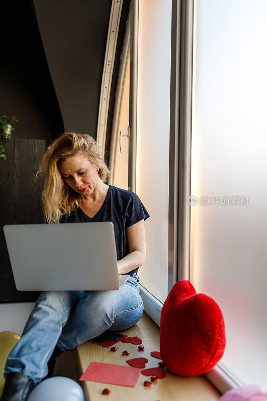 一个女人坐在窗台上，用着笔记本电脑，幻想着她心爱的人