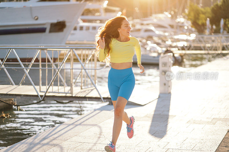 一个女人在海边的路上奔跑。日落时分，女运动员在海边散步道上训练