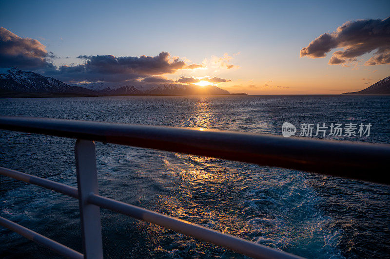 冰岛雪山上的日落，前面是大海，后面是一艘游船，前面是栅栏