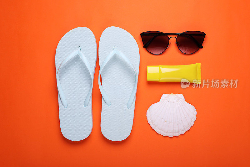 时髦的白色人字拖，太阳镜，防晒霜和橙色背景的贝壳，平躺着