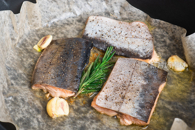 三文鱼排在烤盘纸上，加入迷迭香和大蒜。红鱼肉制作