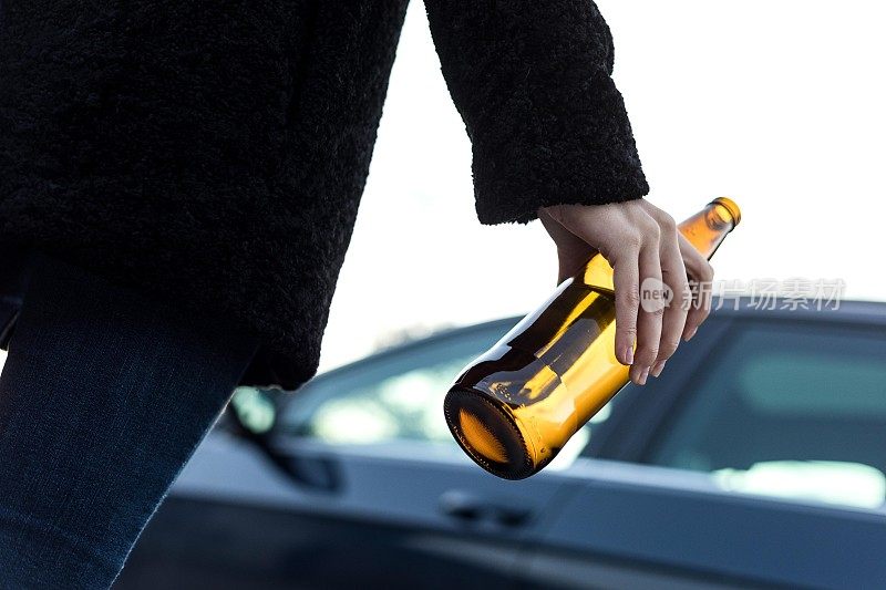 一个喝醉酒的年轻女子拿着一瓶啤酒朝汽车走去。