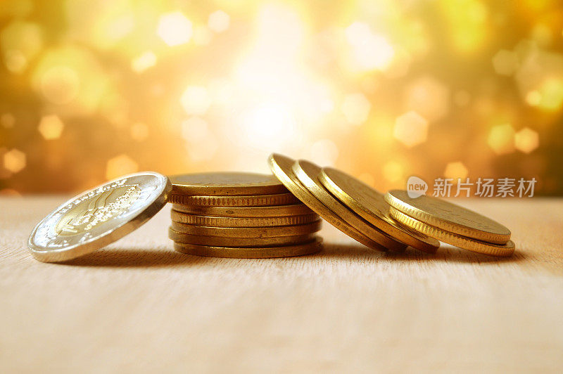 一堆钱的金色金属货币硬币排列成重叠的一套或堆叠或下降塔的硬币放置在木表面与闪闪发光的明亮的金色闪闪庆祝背景的散景灯