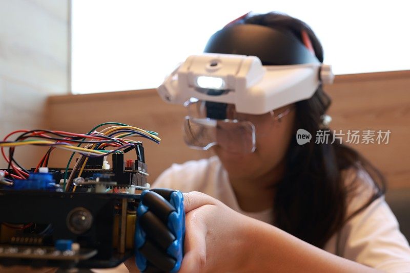 一个可爱的女孩戴着虚拟现实眼镜(VR)头戴式耳机，并在她的虚拟机器人组装上移动她的手。机器人和在家自学