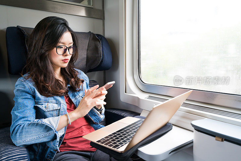 可爱的亚洲女人在火车上使用智能手机和笔记本电脑