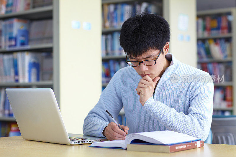 一个用笔记本电脑和书本学习的年轻人