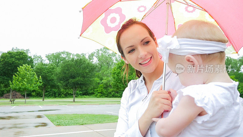 母亲抱着蹒跚学步的女儿和雨伞在雨天的户外