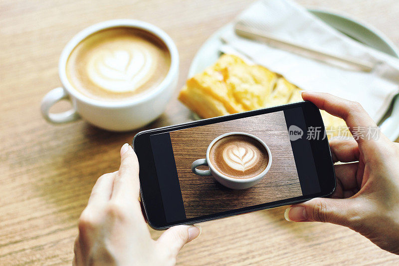 用手机拍摄木桌上的拿铁咖啡杯，咖啡生活方式。