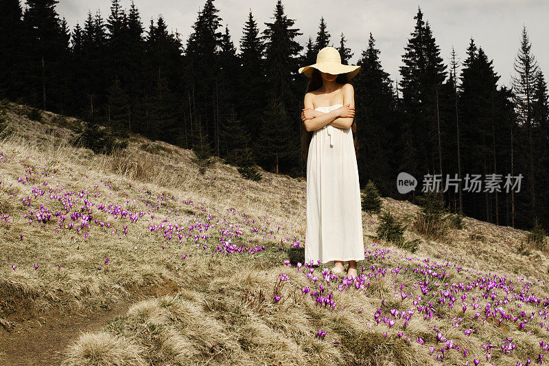 年轻女子站在山中鲜花盛开的山坡上