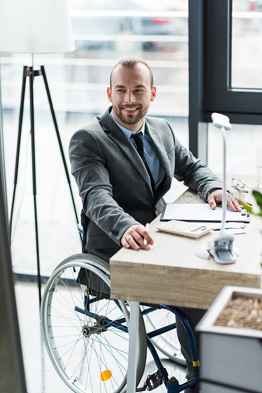 微笑的身体残疾的商人在轮椅上的西装在办公室工作