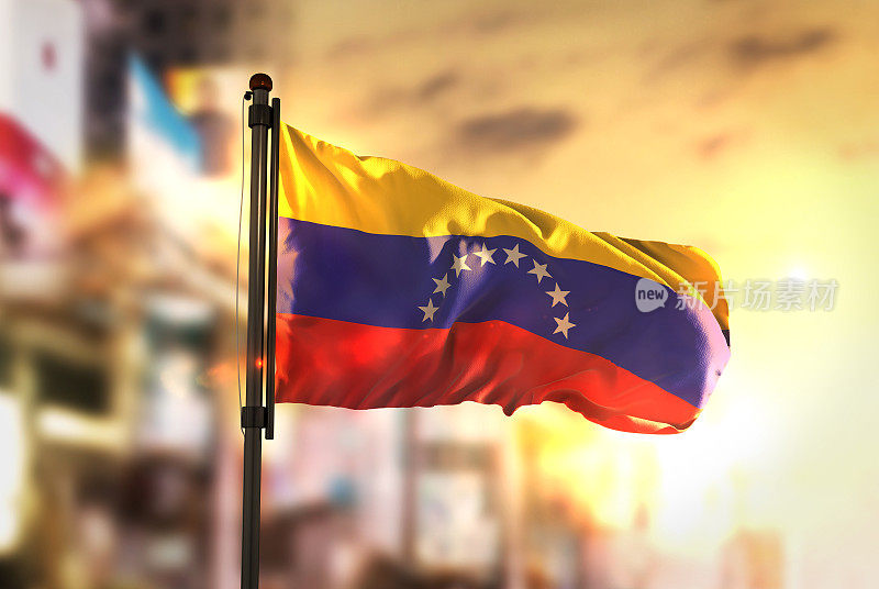在日出的背光下，委内瑞拉国旗对着城市模糊的背景