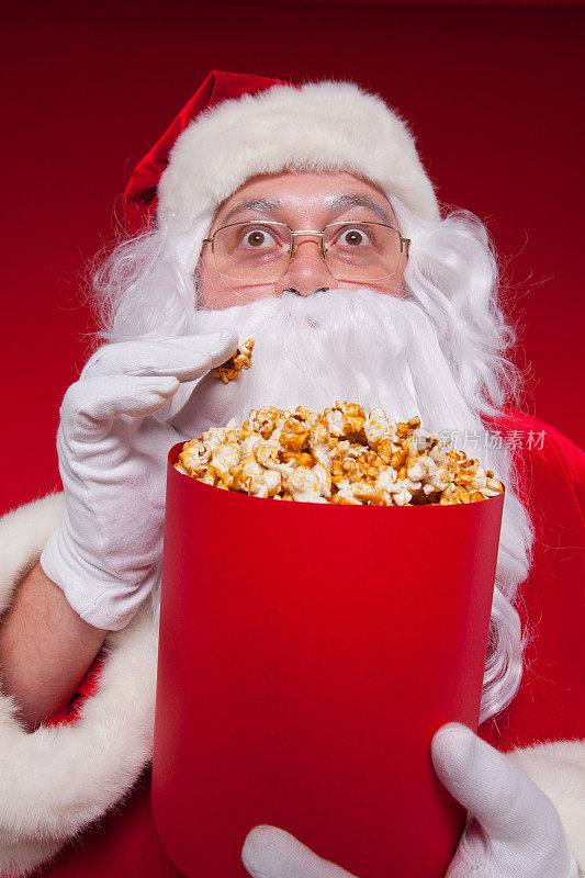 传统圣诞老人看电视，吃爆米花。圣诞节。红色的背景。的情绪。恐惧。惊喜