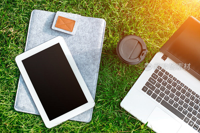 草地上的笔记本电脑，咖啡杯和平板电脑在户外公园
