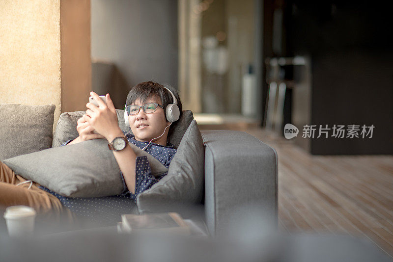 年轻的亚洲男子在沙发上用智能手机听音乐