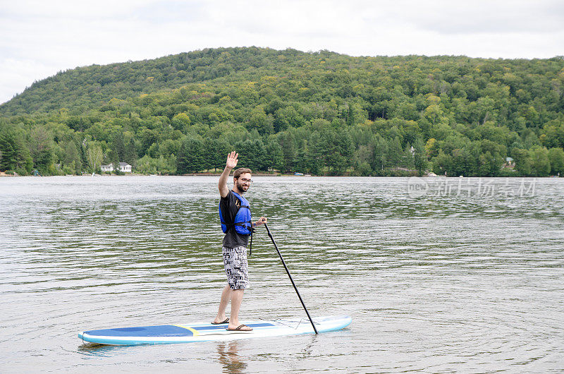 夏日的湖面上，一个年轻人站在桨板上向你挥手